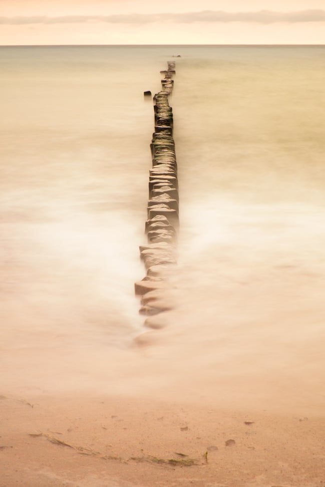 Wooden breakwater on wavy Baltic Sea.  Pink horizon