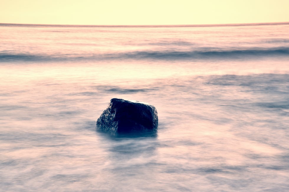 Romantic atmosphere. Boulders sticking out from smooth sea. Pink horizon